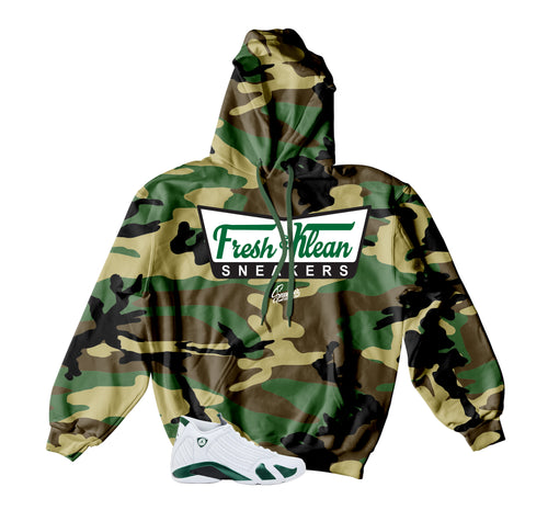 A camouflage pullover hoodie with a green and brown camo pattern, featuring a white chest graphic that reads 'Fresh Mean SNEAKERS' in green and black. A white and green sneaker is shown at the bottom left as a styling prop on a solid white background.